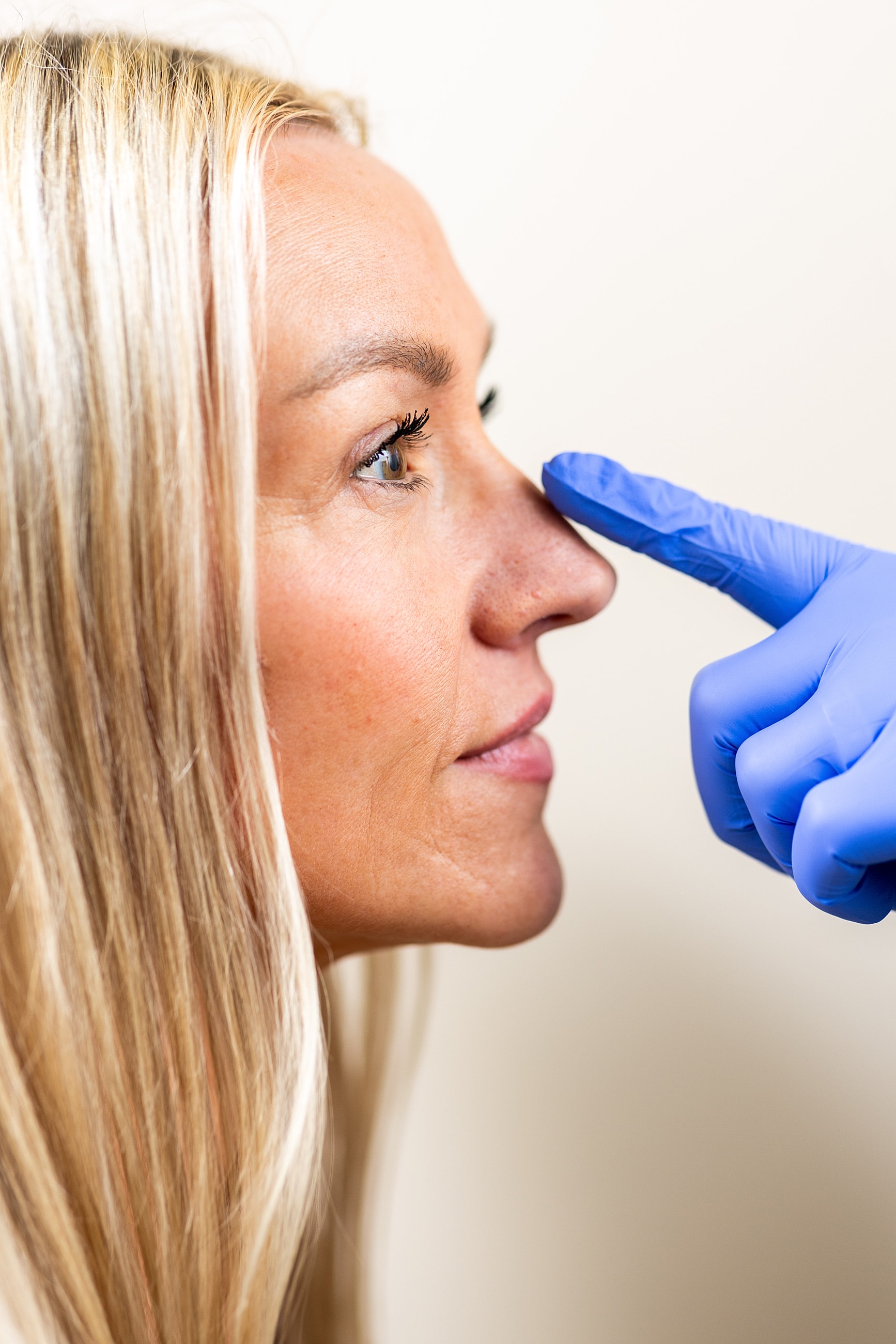 Gloved hand pointing at woman's nose.