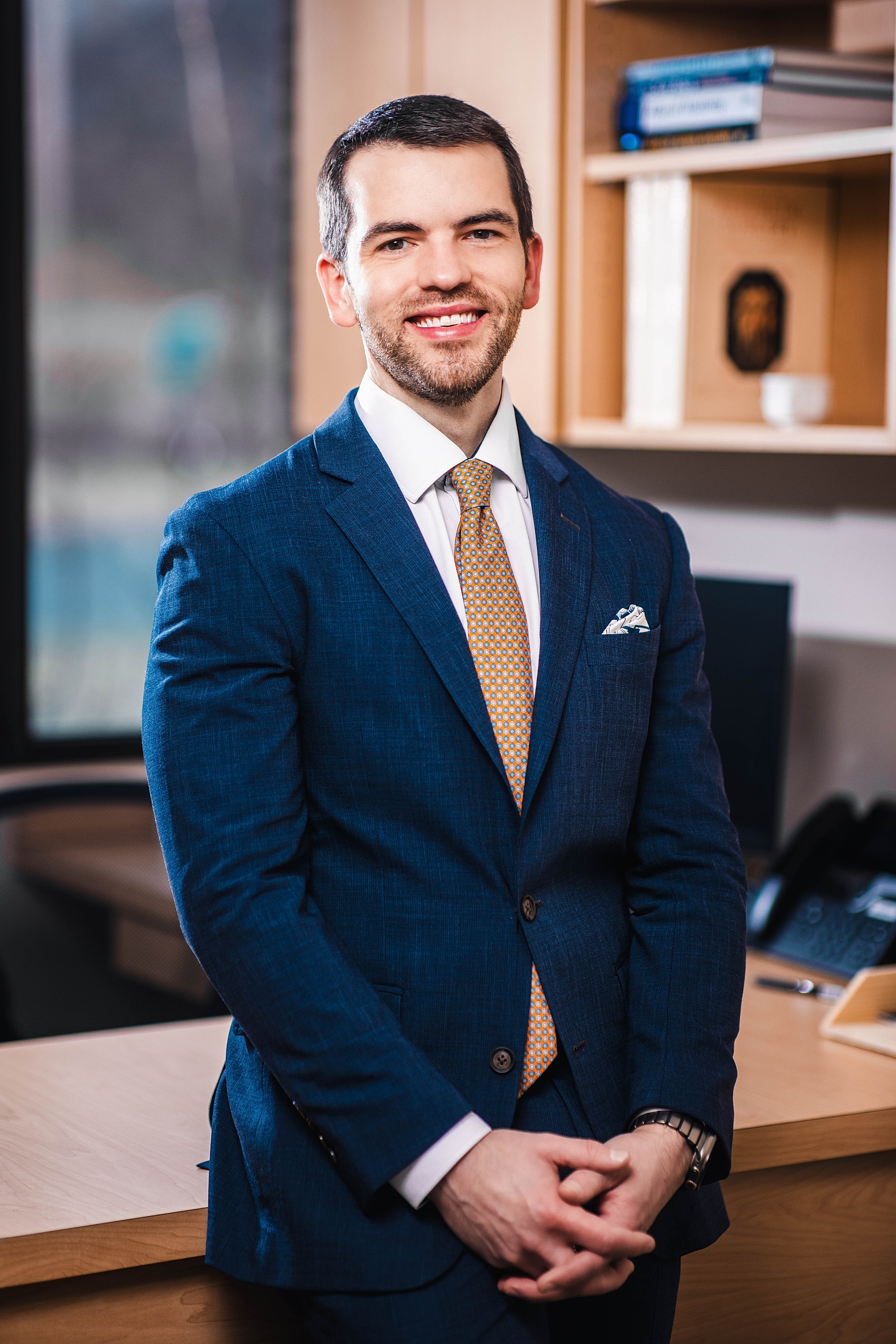 Smiling man in a blue suit, office background.